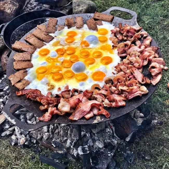 Piknikové raňajky: slanina, vajcia a plátky chleba grilované na žeravom ohništi v prírode.