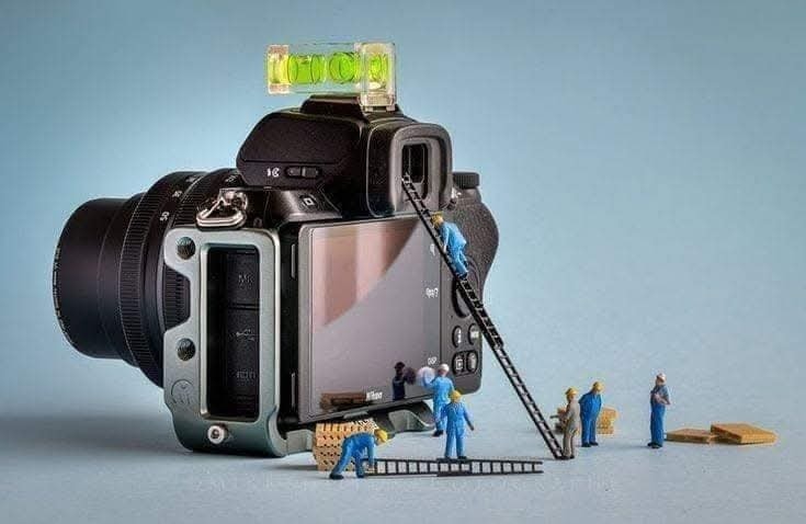 Miniatúrni robotníci opravujúce fotoaparát s vodováhou na vrchu, modrá pozadie. Kreatívna fotografia.