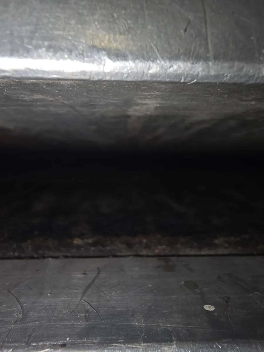 Tmavá štrbina medzi kovovými povrchmi odrážajúca svetlo, zblízka zachytené detaily textúry.