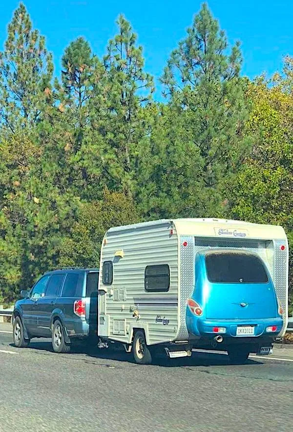 SUV ťahajúci obytný príves po ceste obklopenej borovicami.