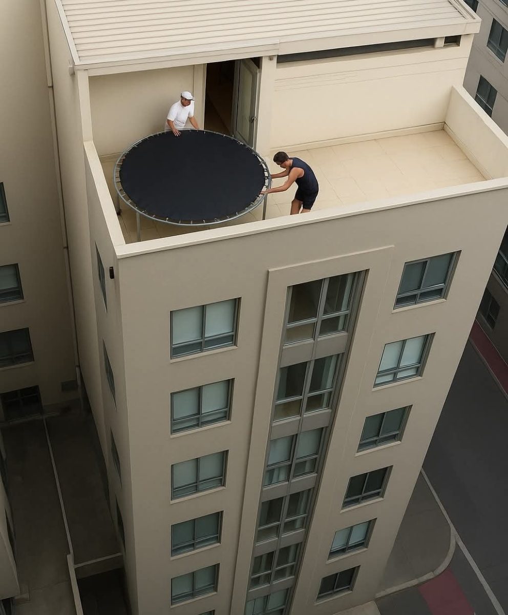 Muž na balkóne mrakodrapu presúva veľkú trampolínu dovnútra cez otvorené dvere.