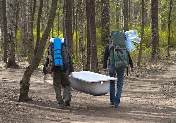 Dvaja turisti nesú vaňu lesom, vybavení batohmi na výlet do prírody.