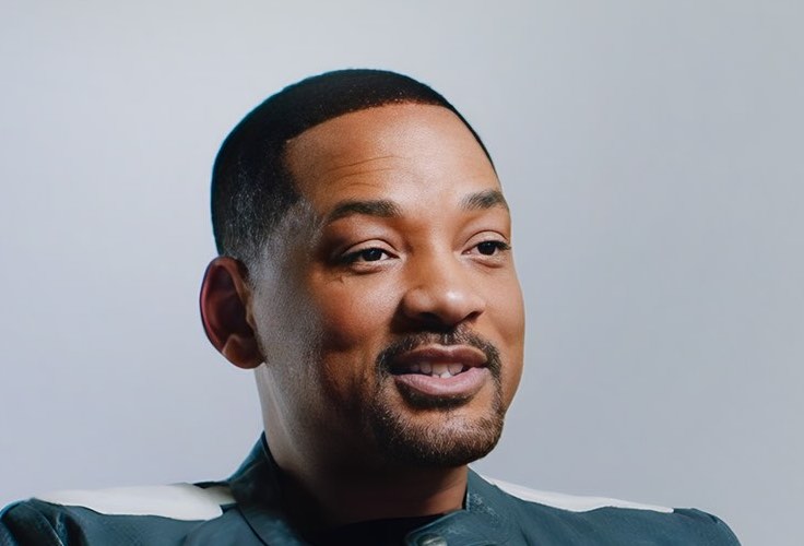 Osoba s krátkymi čiernymi vlasmi a bradou, usmievajúca sa, oblečená v tmavom oblečení, neutrálne pozadie.