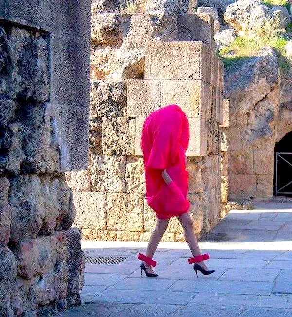 Módny model v ružovom šate s vysokými opätkami v historickej kamennej lokalite.