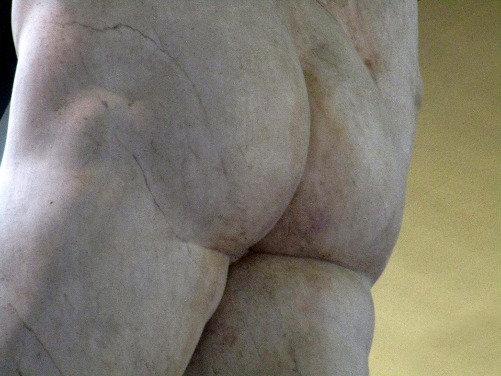 Socha Michelangelovho Dávida zblízka, zameraná na detail zadnej časti, ukazuje majstrovstvo renesančného sochárstva.