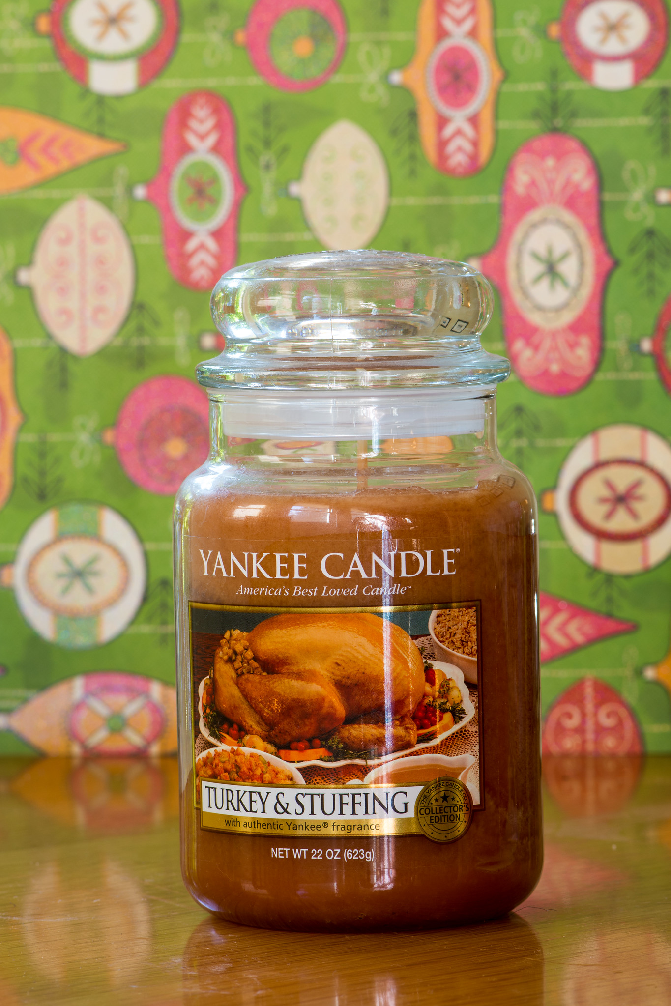 Sviečka Yankee Candle s vôňou moriaka a plnky na drevenom stole pred farebným, retro pozadím.