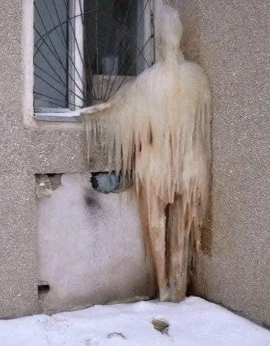 Ľadová socha pripomínajúca postavu pri okne budovy, zamrznutá počas zimy.