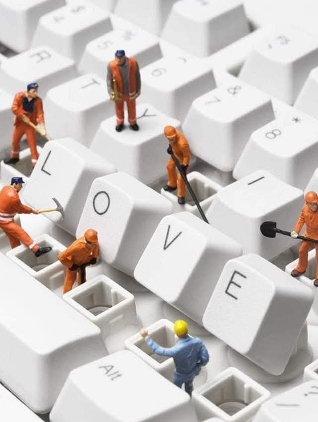 Miniatúrni robotníci skladajú slovo LOVE na klávesnici. Kreativita a láska v digitálnom svete.