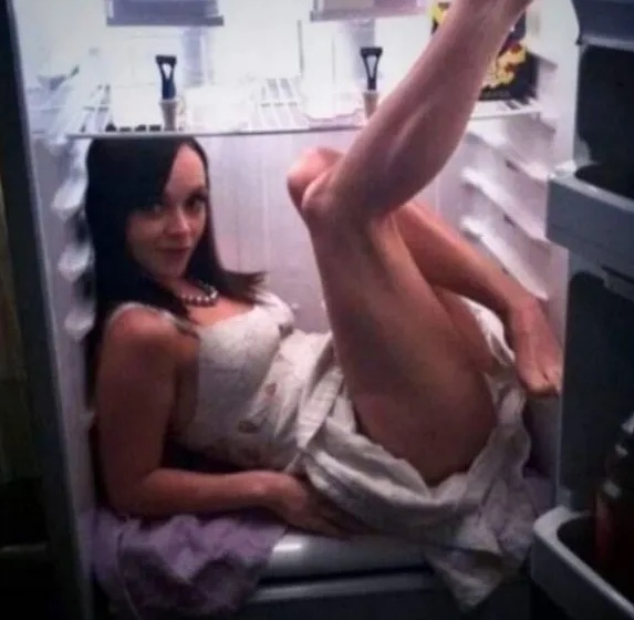 Žena v bielej šatke sedí v chladničke, ukazujúcej nápaditý spôsob úspory miesta.