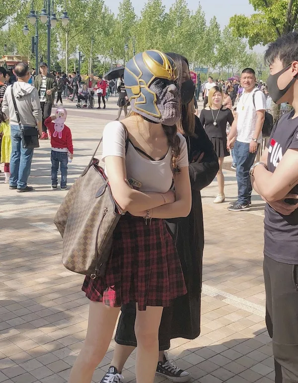 Osoba nosí masku Thanos v parku, okolo sú ľudia a stromy, slnečný deň.