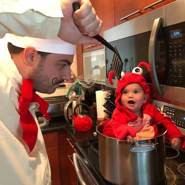 Kuchár a dieťa v kostýme humra v hrnci na sporáku, vtipná scéna v kuchyni.