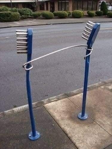 Stojan na bicykle v tvare obrovských zubných kefiek pri ceste na chodníku.