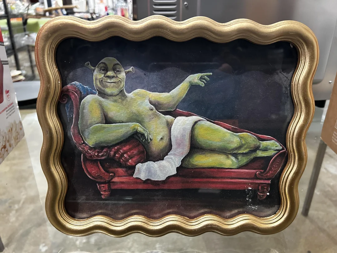 Ogr v zarámovanej podobe slávnej maľby ležiace na červené pohovke s bielym závojom.