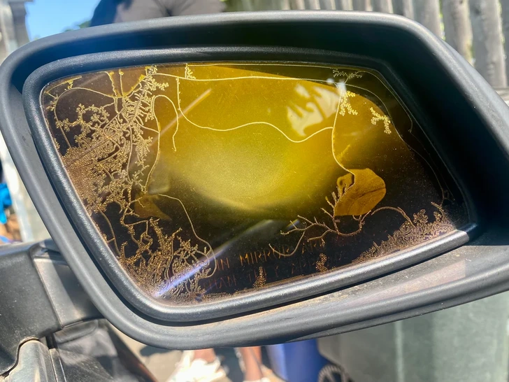 Zrkadlo auta s nezvyčajnými vzormi na povrchu, odražajúce slnečné svetlo.