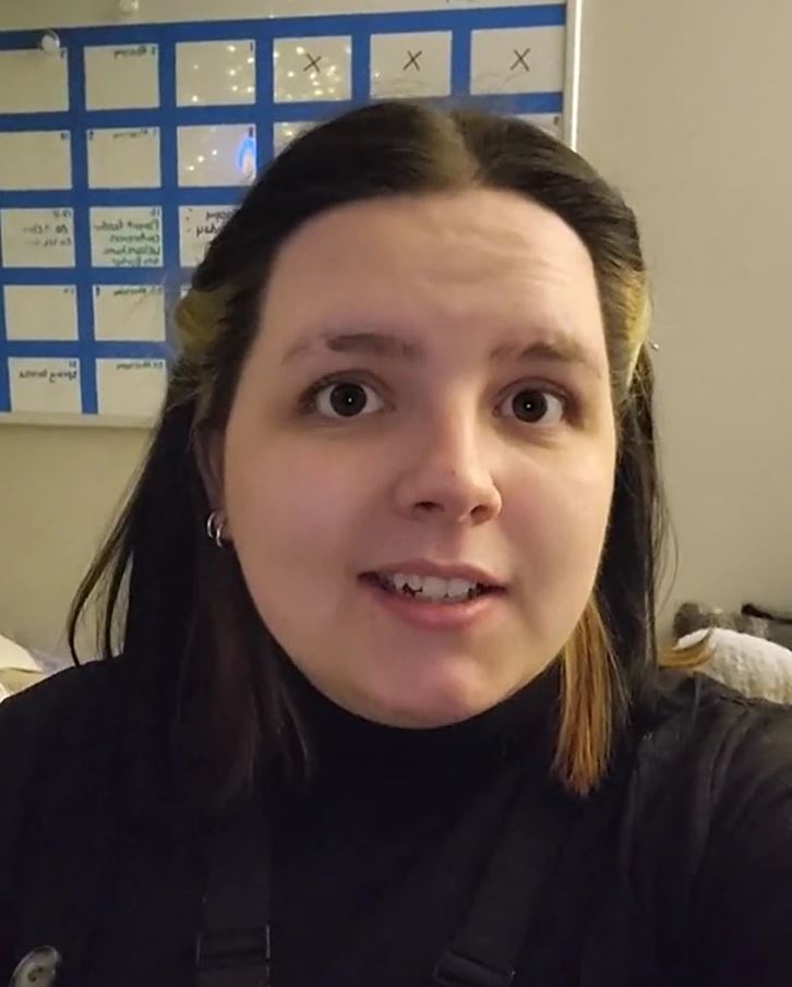 Osoba pred kalendárom na stene, tmavovlasá, v interiéri.