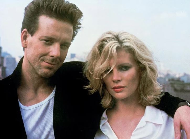 Dvojica v mestskom prostredí: muž v čiernom saku, žena v bielej košeli, pozadia mestské budovy.