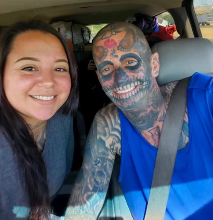 Ľudia vo vozidle s výraznými tetovaniami a batožinou v pozadí na ceste.