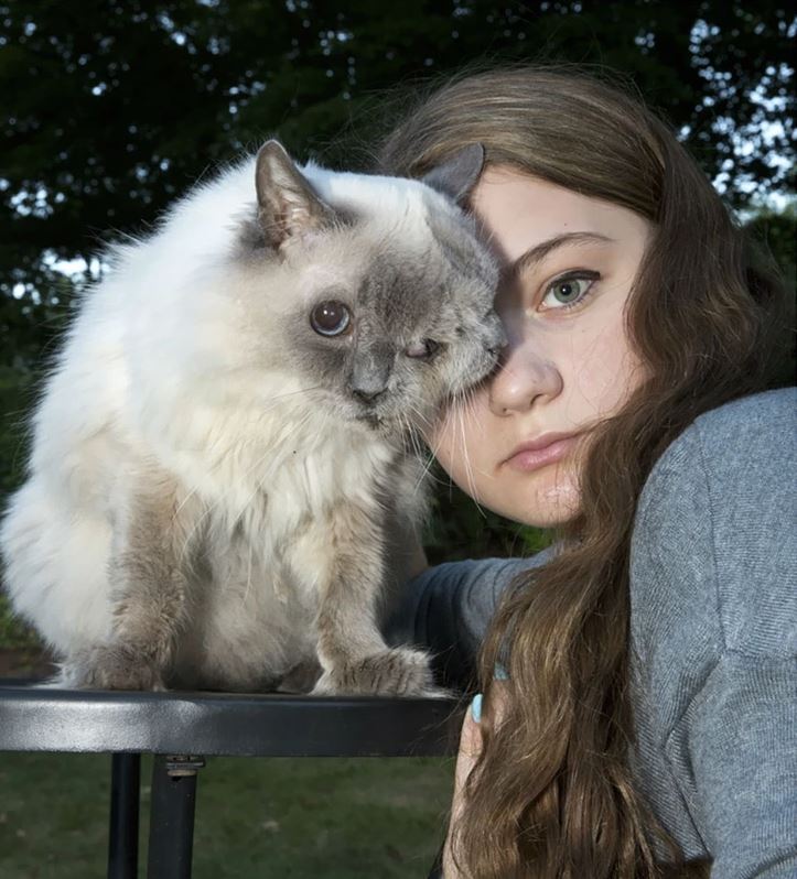 Dievča s dlhými vlasmi pózuje s mačkou na vonkajšej fotografii.