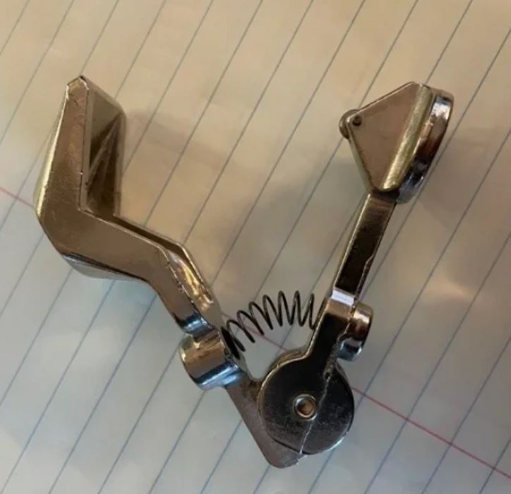 Kovový nástroj s pružinou na riadkovanom podklade.