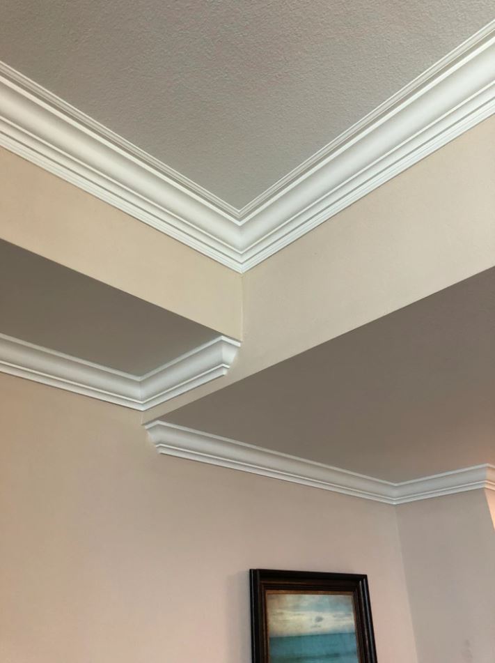 Dekoratívna stropná lišta v interiéri, elegantná biela rímsa s jemnými detailmi na béžovej stene.