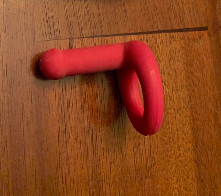 Červený gumový háčik na drevených dverách, moderný dizajn a praktické využitie pre domácnosť.