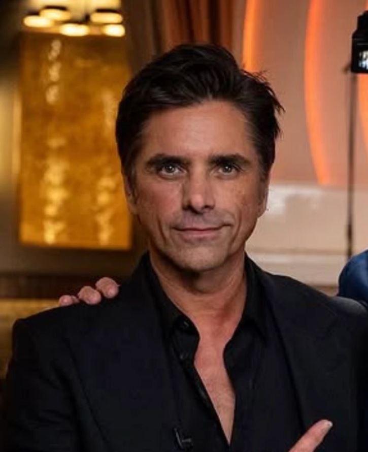 Loftové prostredie s mužom v elegantnom čiernom saku, teplé osvetlenie v pozadí.