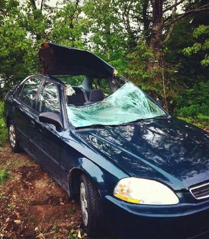 Osobné auto s poškodeným strešným krokom a rozbitým čelným sklom, zaparkované v lesnom prostredí.