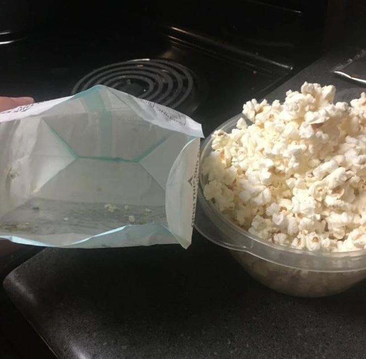 Prázdny sáčok od popcornu vedľa preplnenej misky s čerstvým popcornom na kuchynskej linke.