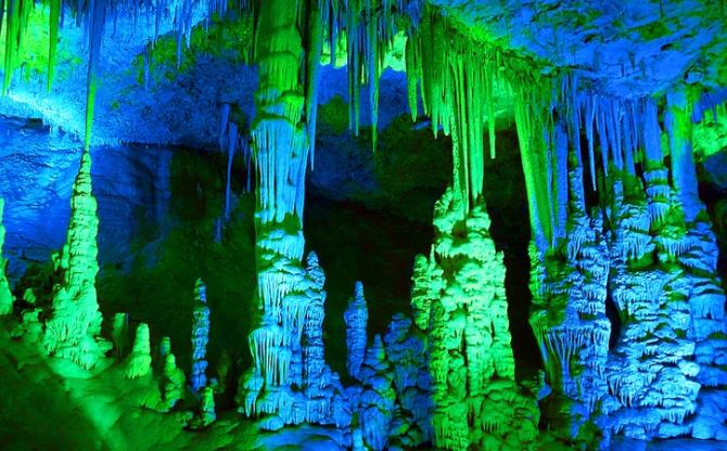 Záhadná jaskyňa s farebnými stalagmitmi a stalaktitmi osvetlená modrou a zelenou. Fascinujúci podzemný svet.