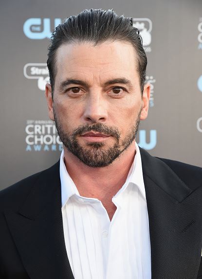 Ospravedlňujem sa, neviem, kto je na tomto obrázku. Popis obrázku: Muž v obleku na červenom koberci, kritické ocenenia na pozadí.