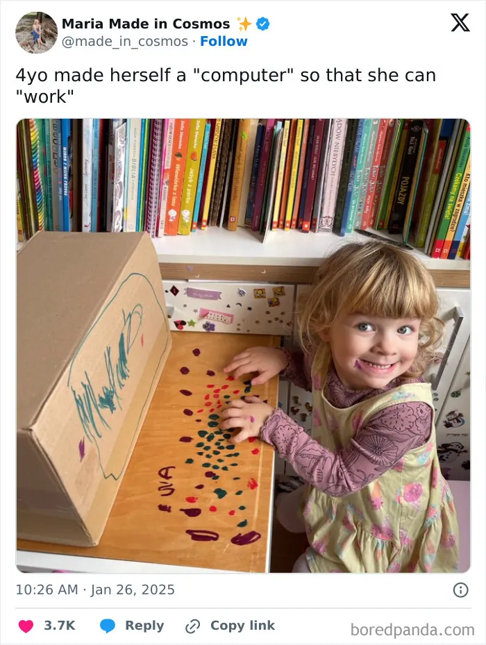 Dieťa sa hrá s kartónovým počítačom, ako keby pracovalo, na stole pred zbierkou kníh.