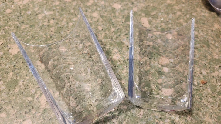 Dva rozbité poháre na zelenej kuchynskej doske, detailný pohľad.