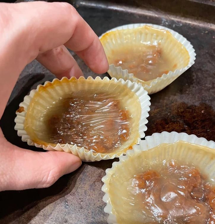 Ruka drží pečený koláčik v papierovej košíčku na plechu.