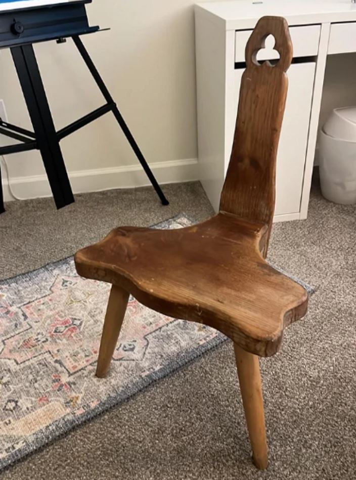 Drevená ručne vyrezávaná stolička s neobvyklým tvarom, umiestnená na koberci v modernej miestnosti.