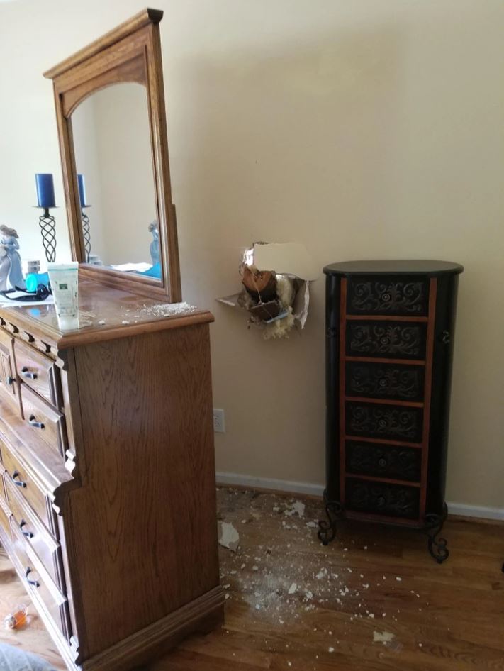 Diera v stene vedľa skrine, rozbité omietky a úlomky na podlahe, chaos v spálni.