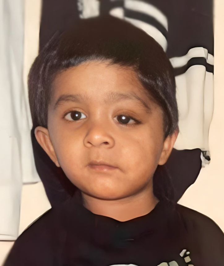 Odfotené dieťa s vážnym výrazom tváre, čierne vlasy a tmavé šaty, na jemne rozostrenom pozadí.