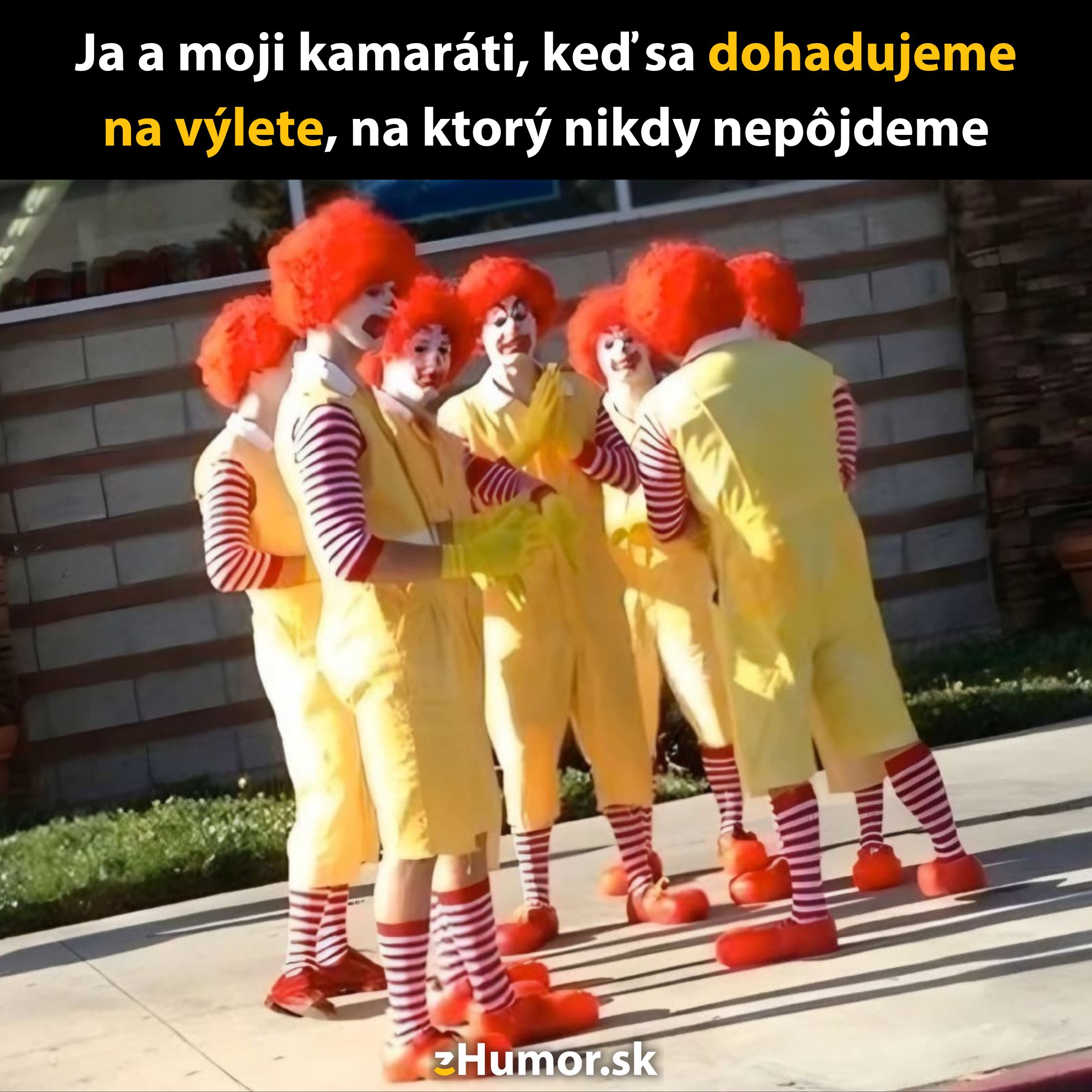 Skupina klaunov v žltých kostýmoch a červených parochňach stojí v kruhu na slnečnej ulici.