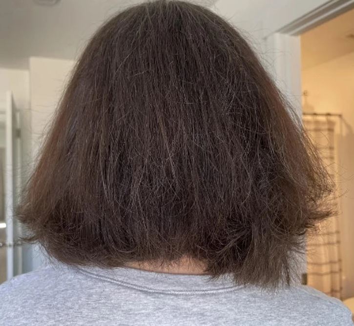 Žena s krátkymi, hnedými vlasmi v interiéri, pohľad zozadu na nový zostrih vlasov.