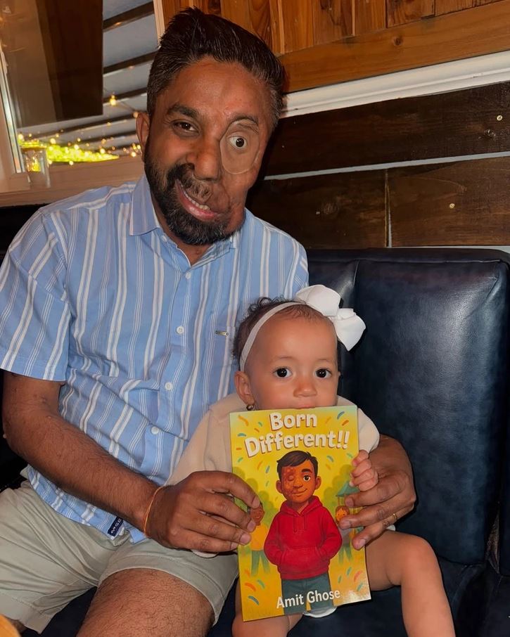 Osoba sediaca s dieťaťom drží knihu Born Different!! a usmieva sa na kameru.