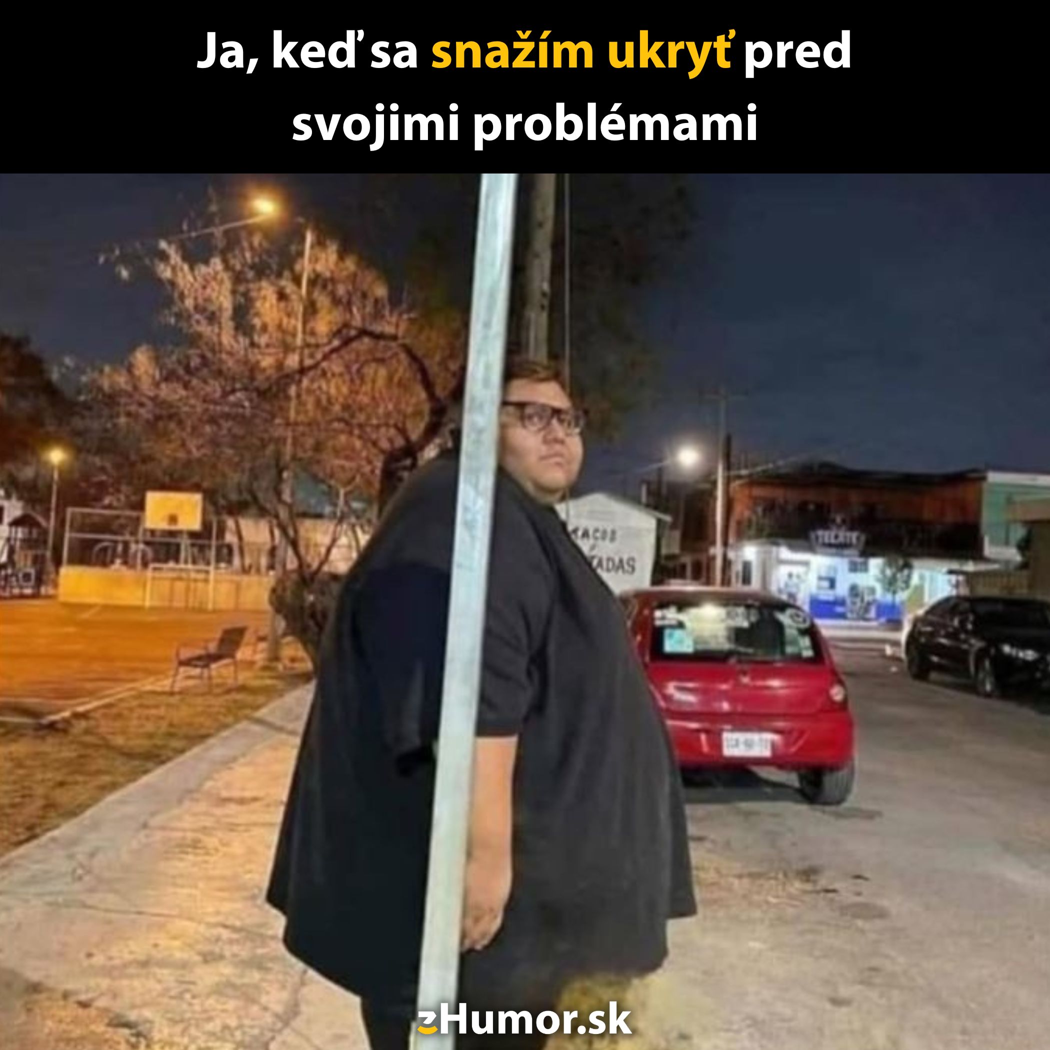 Osoba sa komicky skrýva za stĺpom na ulici v noci, humoristický moment.