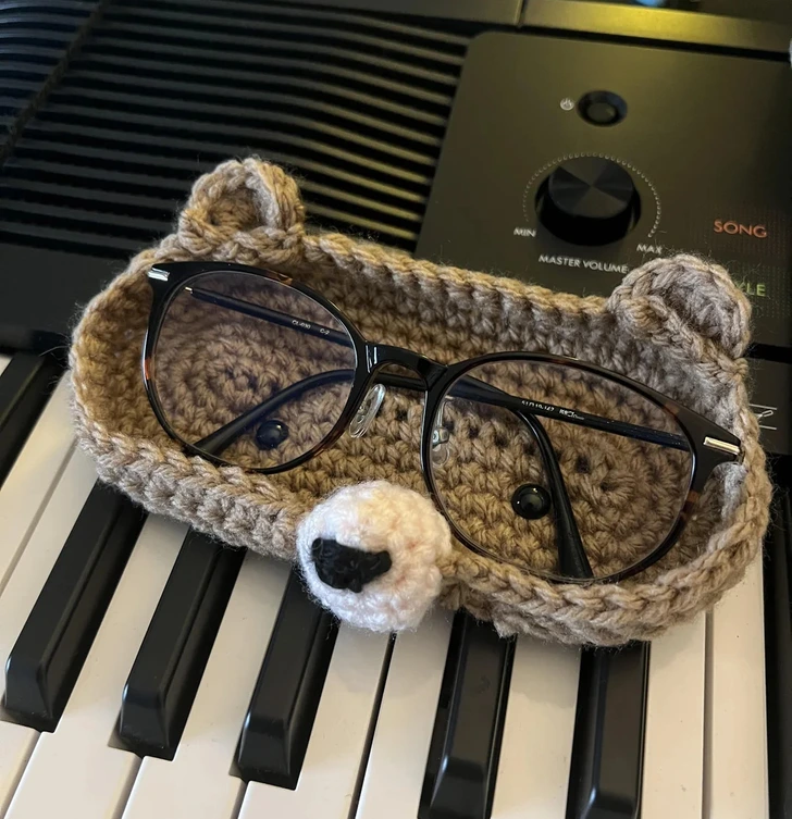 Háčkovaný obal na okuliare v tvare medveďa leží na klávesnici piano.