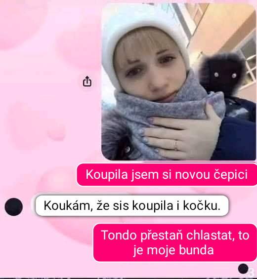 Žena v novej čiapke drží šál pred budovou; humorný textový výmena o mačke a bunde.