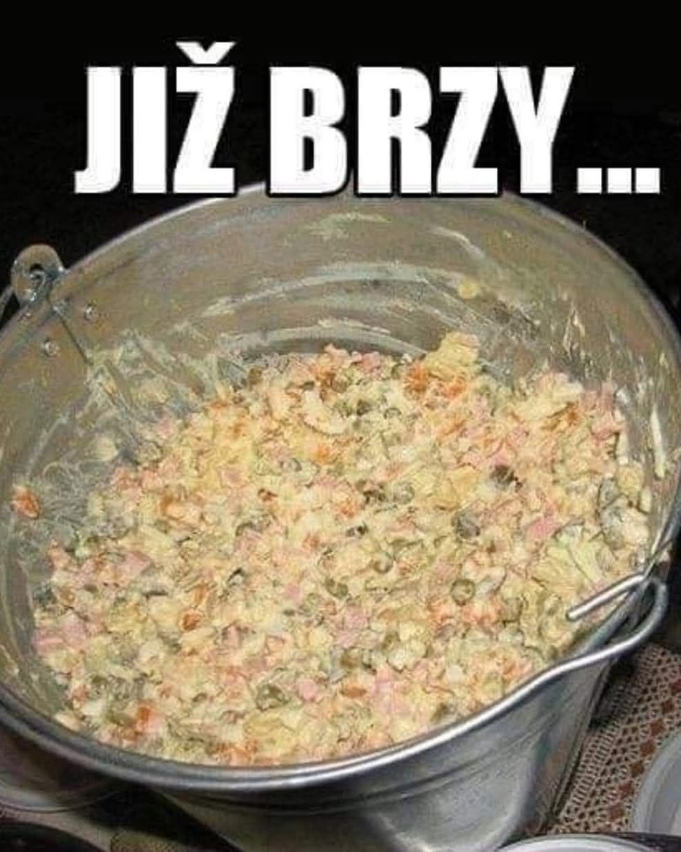 Vedro plné zemiakového šalátu pripraveného na jedlo, s nápisom JIŽ BRZY v hornej časti obrázka.