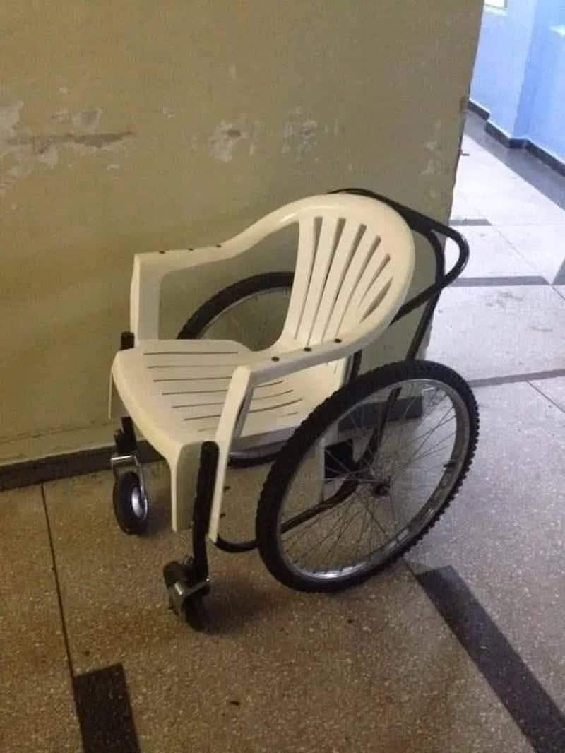 Plastová stolička spojená s kolesami, vytvára provizórny invalidný vozík na chodbe.