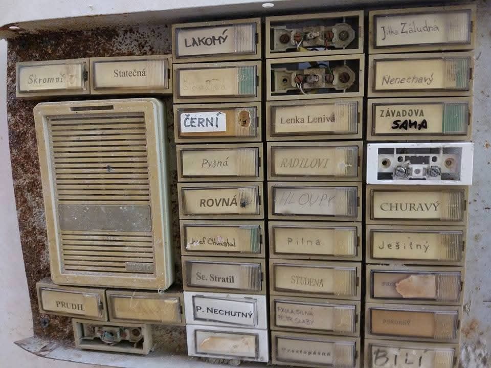 Opis opotrebovaných zvončekov s rôznymi priezviskami na staršej budove, niektoré sú poškodené alebo rozbité.