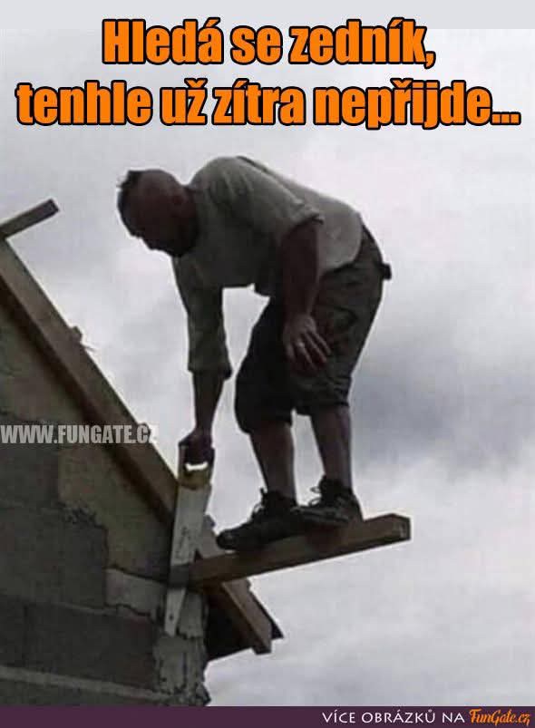 Muž na stavbe, stojaci na doske, sa pokúša rezať ju pílkou, čím ohrozuje svoju bezpečnosť.