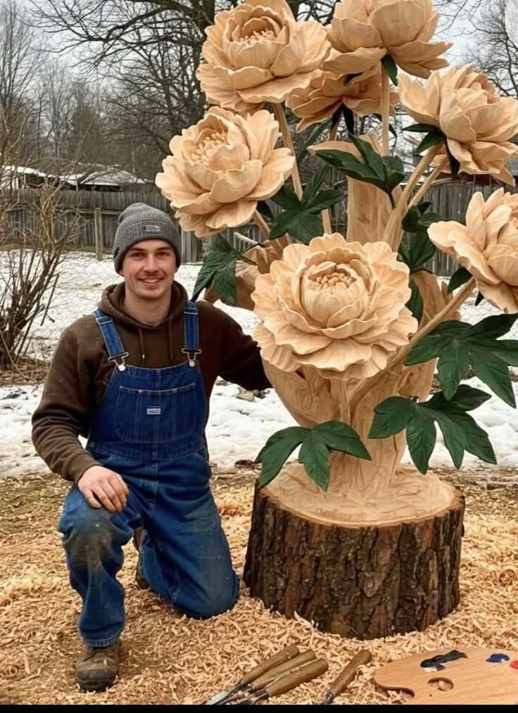 Muž pri drevorezbe kvetov na pni v zimnej záhrade, oblečený v montérkach a čiapke.