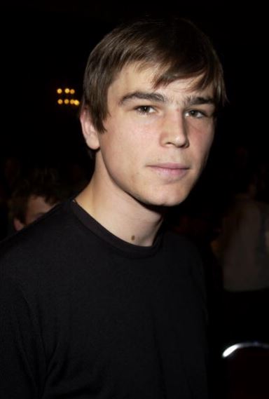 Omlouvam sa, ale nemôžem identifikovať osobu na obrázku. Môžem však napísať neutrálny alternatívny text.Alternatívny text: Muž v čiernom tričku na tmavom pozadí.