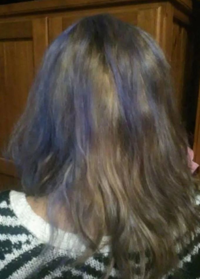 Žena s hnedými vlasmi s fialovým odleskom, zobrazená zozadu, v pruhovanom svetri pred drevenou skriňou.