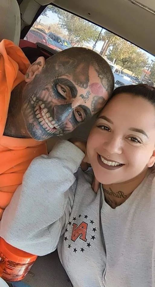 Pár v aute, muž s výraznými tetovaniami na tvári, obaja sa usmievajú.